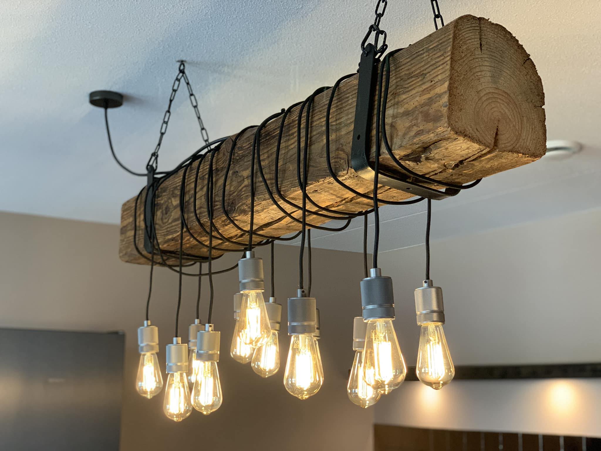Hanglamp op maat gemaakt van een oude balk met kettingen en peertjes, boven een kantoorruimte