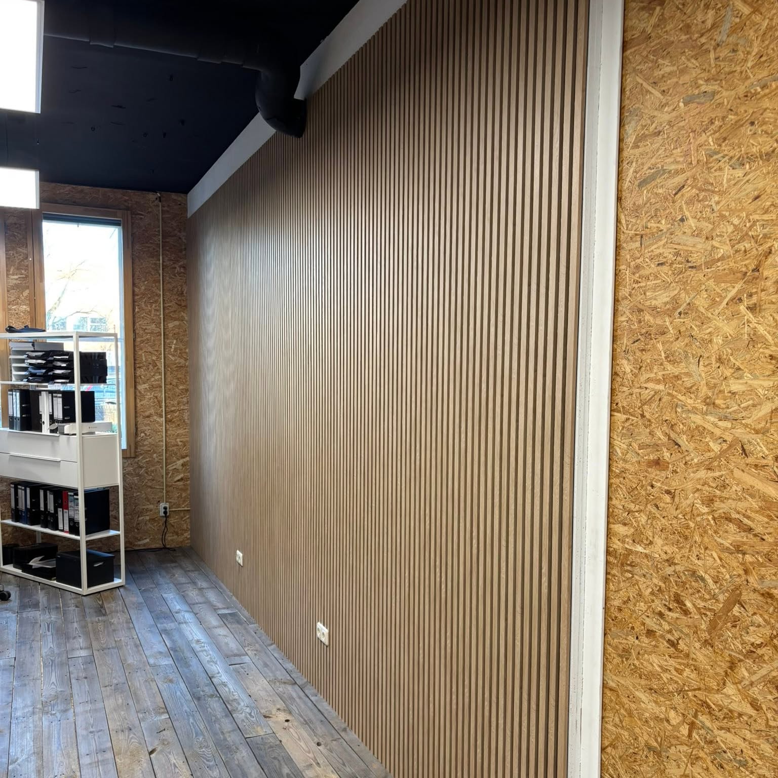 Eiken lamellenwand langs een gang, naast OSB-beplating en een oude planken vloer