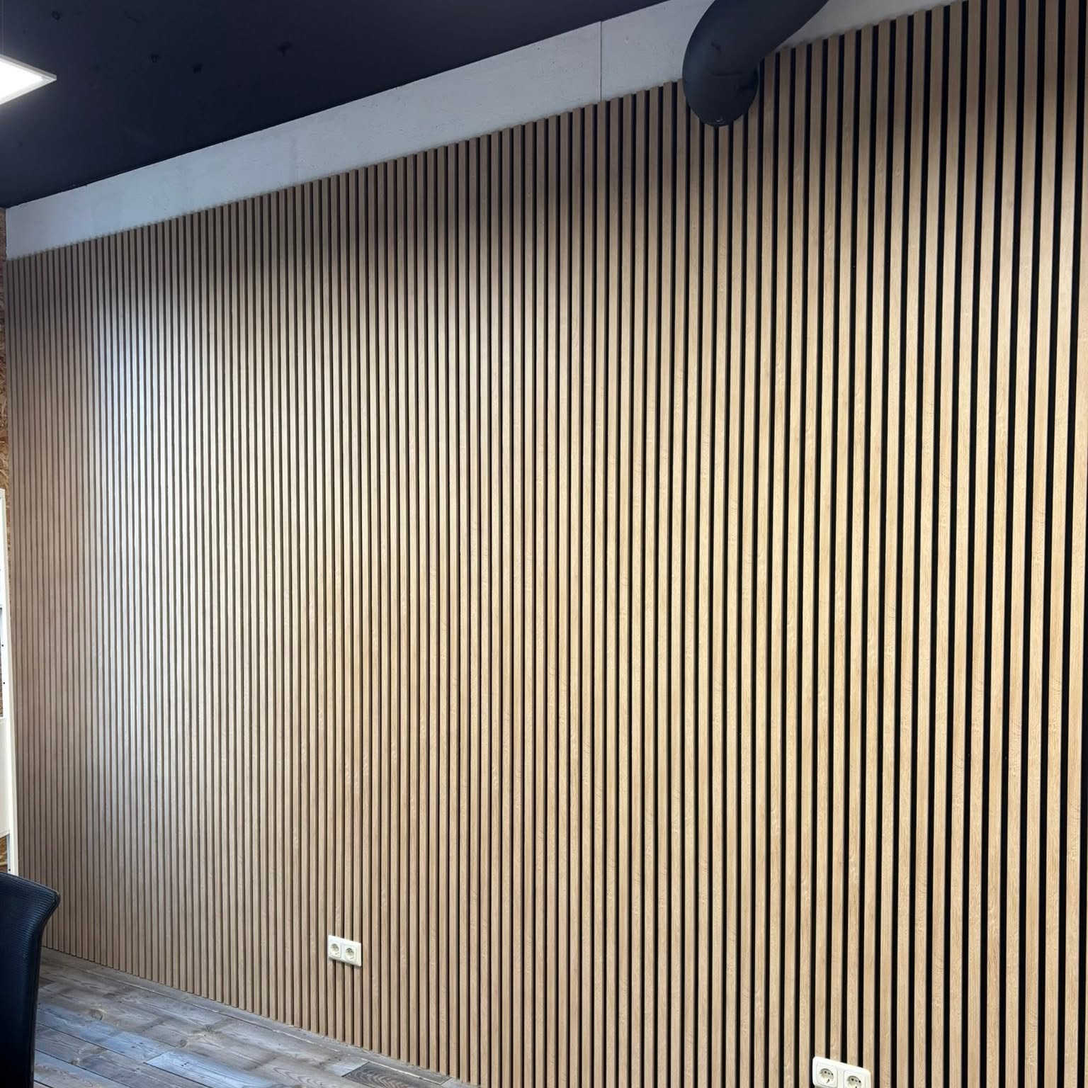 Eiken lamellenwand van vloer tot plafond tegen een zwart plafond