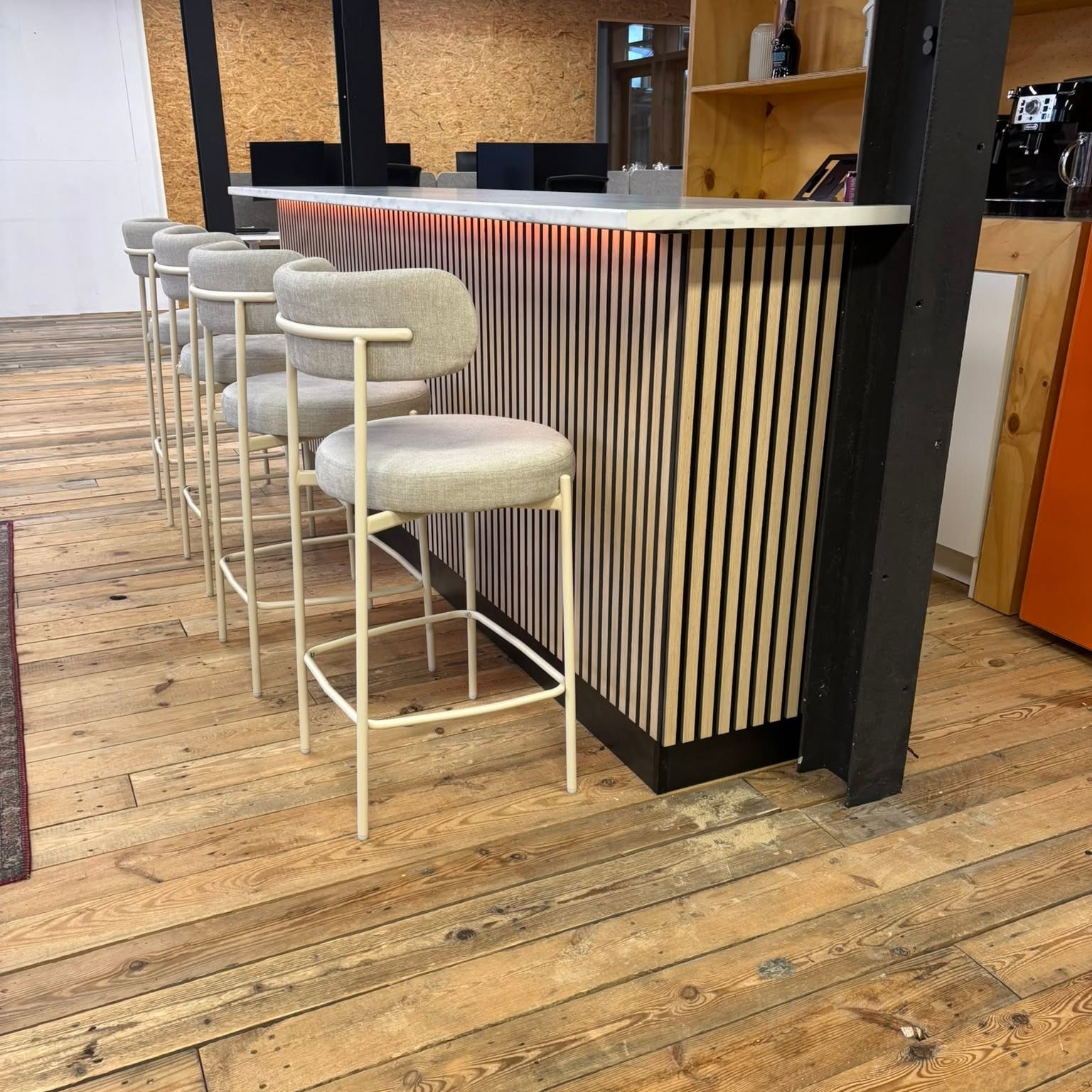 Bar met eiken lamellenfront, marmeren blad en warme verlichting, met vier barkrukken ervoor